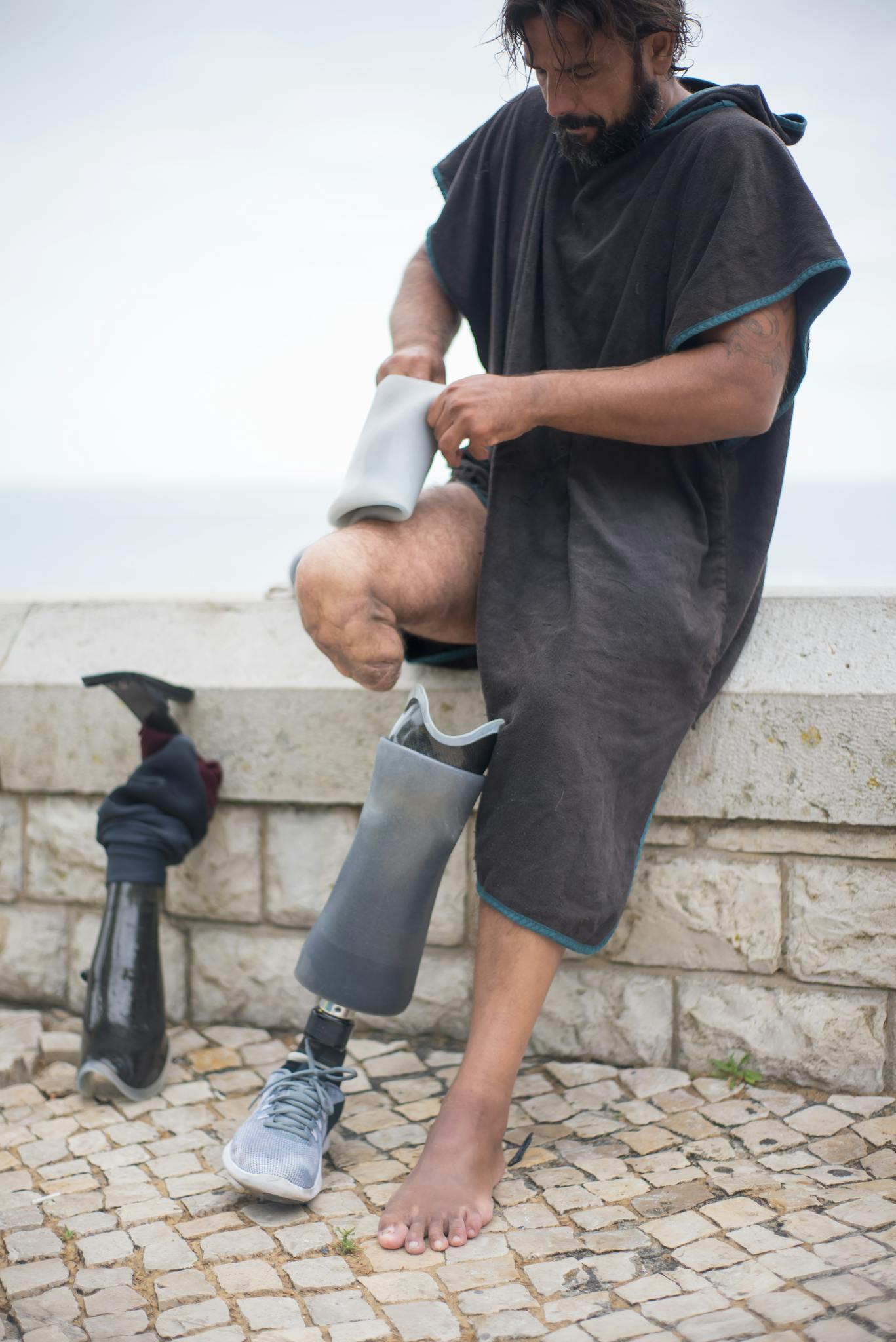 A man adjusting his prosthetic leg by the seaside, showcasing independence and adaptability.