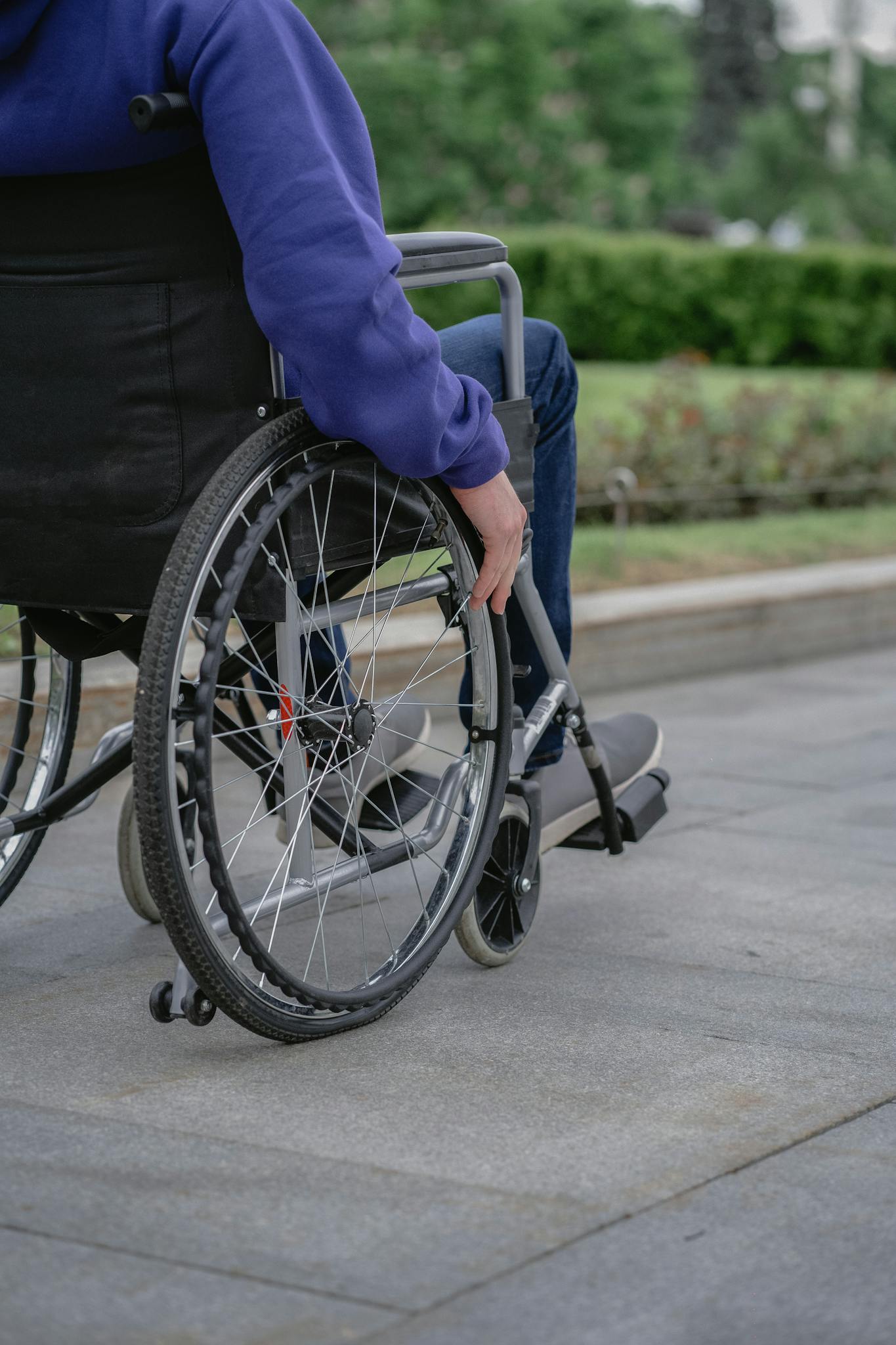 Individual in a wheelchair on a paved walkway outdoors, showcasing mobility and independence.