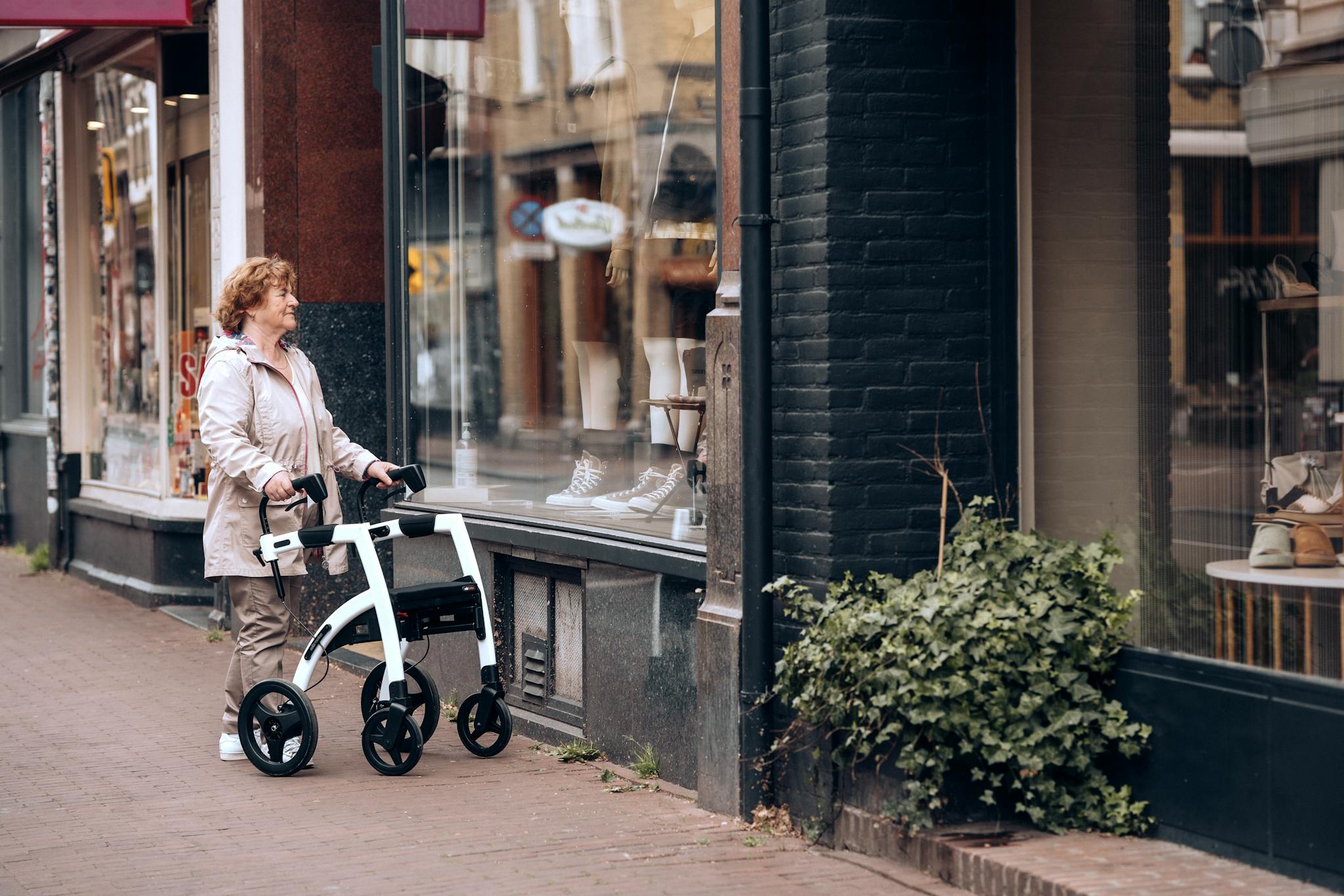 Senior woman with a rollator walker window shopping in Amsterdam's urban street.